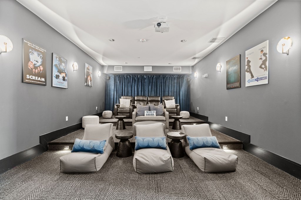 A room with grey walls and a carpeted floor has a row of white chairs with blue pillows.