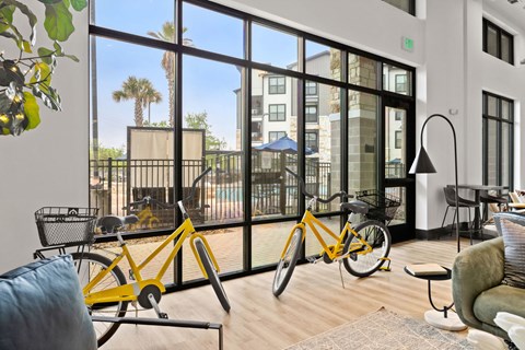 A yellow bicycle is leaning against a wall in a room with a view of a pool and palm trees.