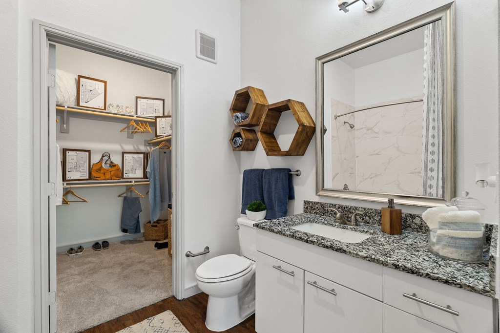 A bathroom with a white toilet, a mirror, and a shelf with various items.