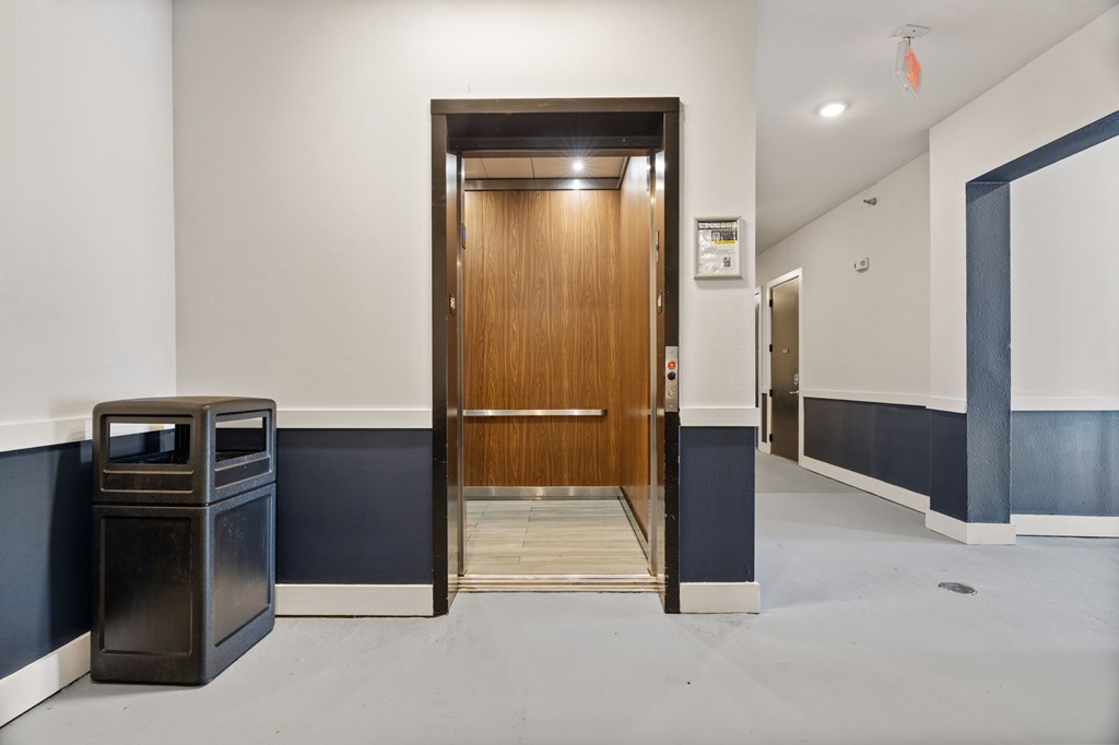 A hallway with a wooden door and a trash can.