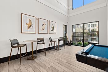A pool table is in the middle of a room with chairs and pictures on the wall.