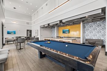 A pool table is in the middle of a room with a bar and a television.