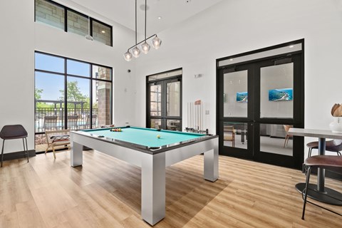 A pool table in a room with a view of a fence and trees outside.