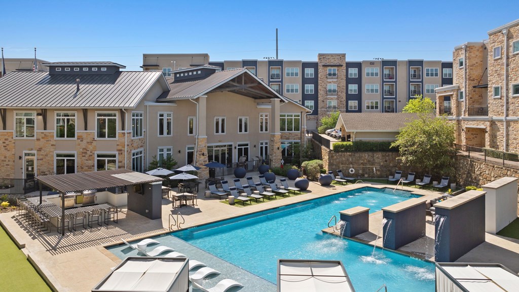 A large swimming pool surrounded by lounge chairs and umbrellas in front of a building.