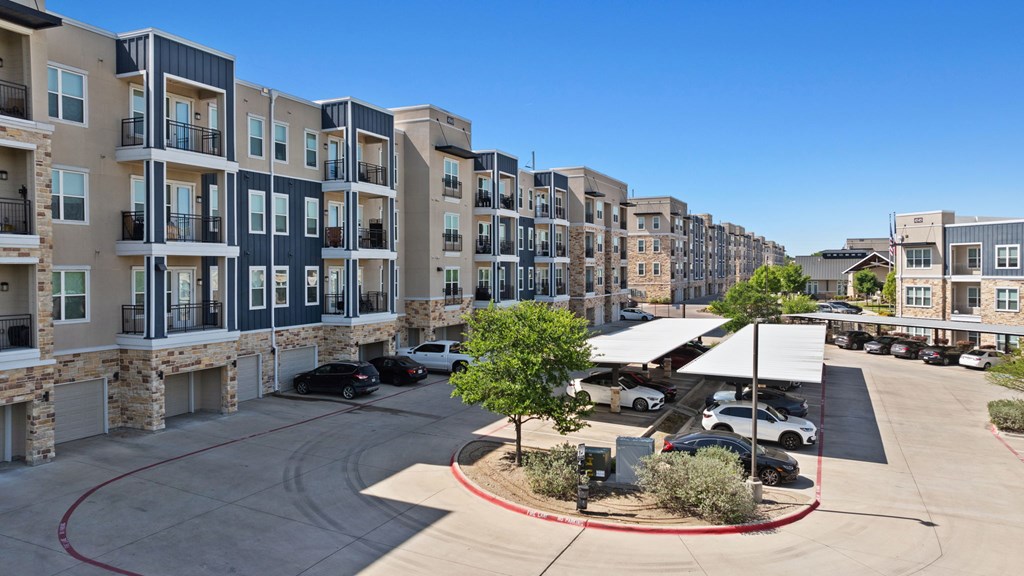A view of apartment buildings with cars parked in the driveway.