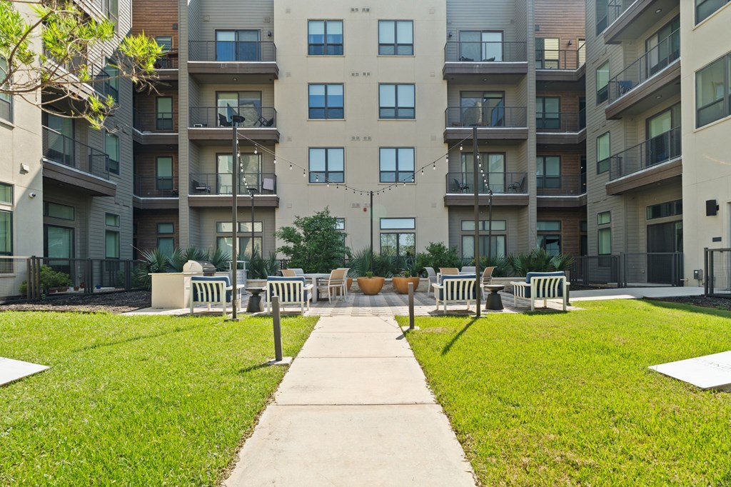 A concrete walkway leads to a grassy area with benches in front of apartment buildings.