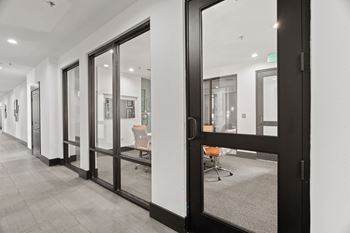 A hallway with a glass door leading to a room with a chair and a table.