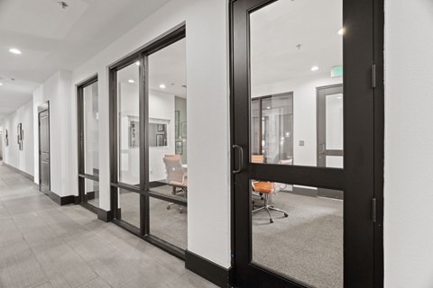 A hallway with a glass door leading to a room with a chair and a table.