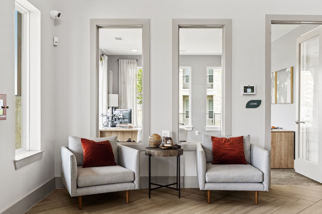 Two grey chairs with red pillows are in a room with white walls.