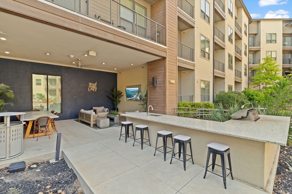 A patio with a bar and stools is surrounded by apartment buildings.