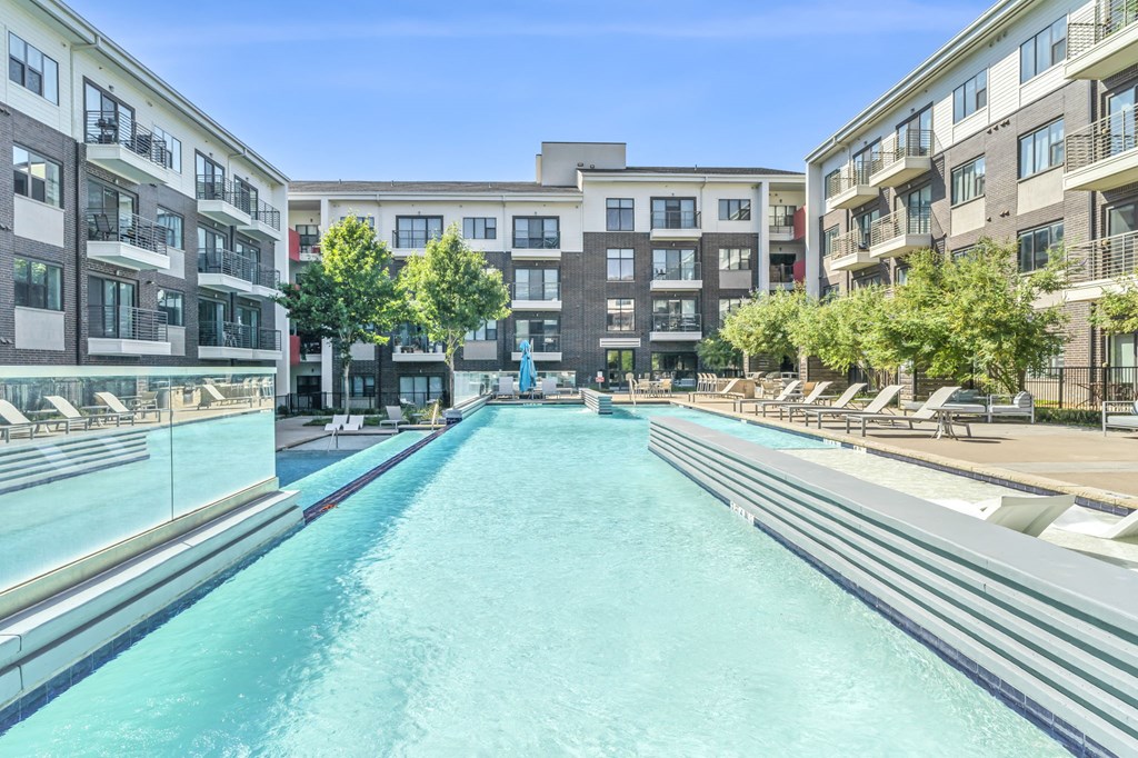 a swimming pool with chaise lounge chairs and trees in front of an apartment building