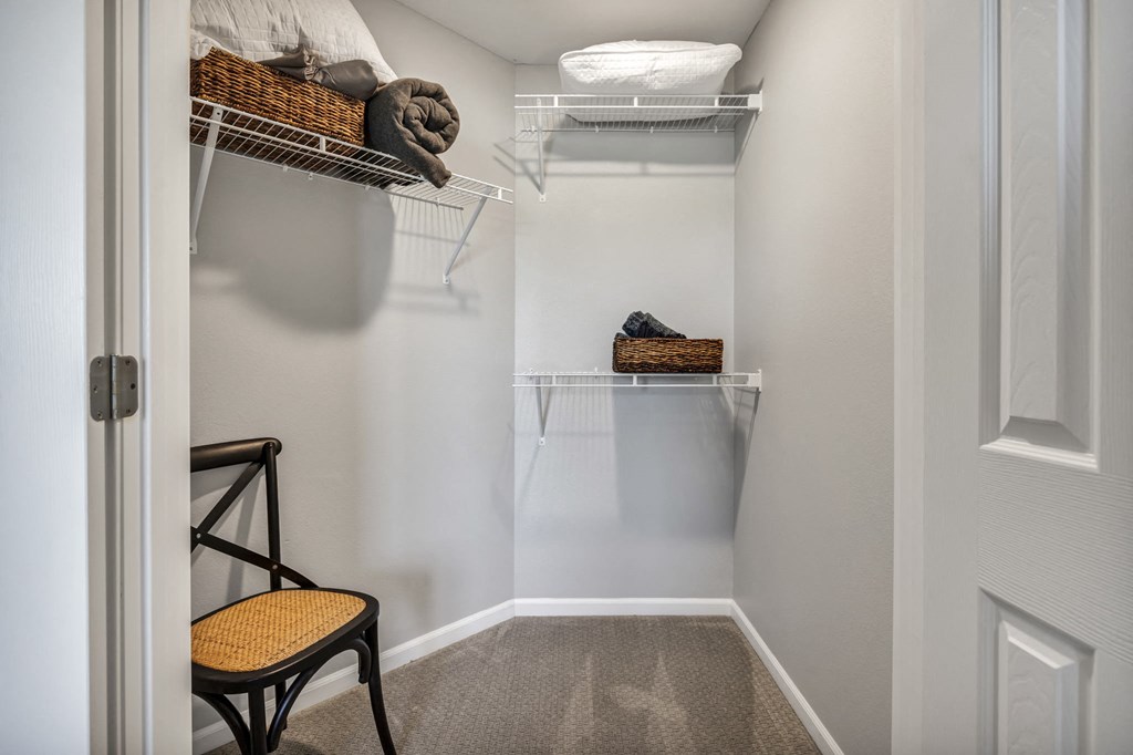a walk in closet in a home with white walls and shelves and a white door