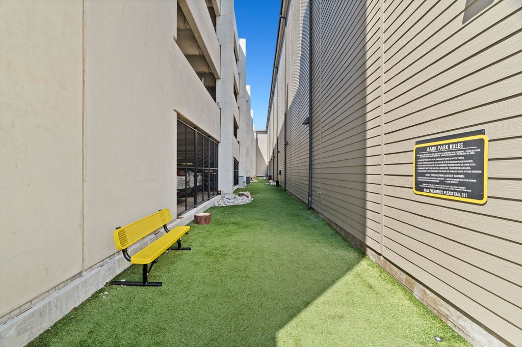 A yellow bench sits on a green lawn next to a building.