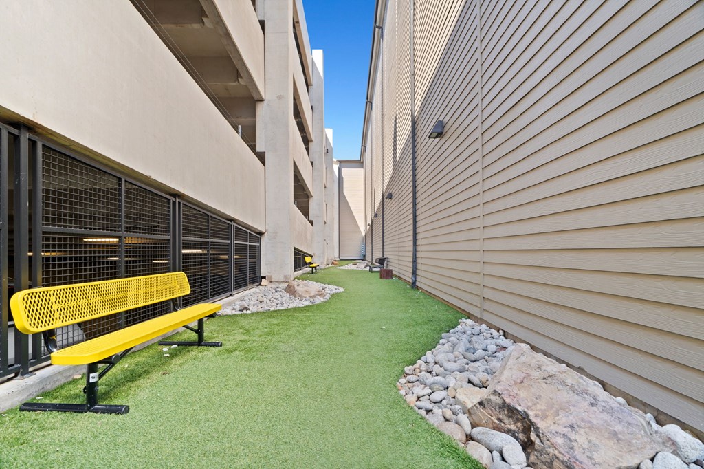 A yellow bench sits on a green lawn in front of a building.