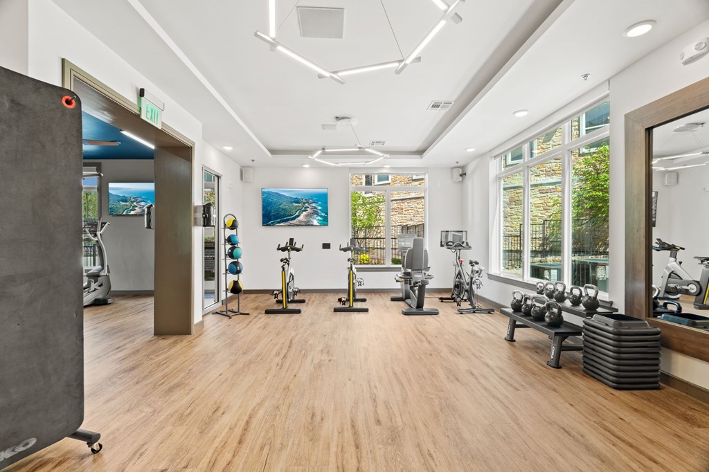 A gym with a variety of exercise equipment and a view of the outdoors through the windows.