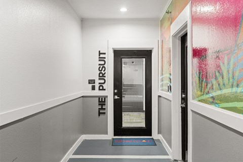 A hallway with a black door and a sign that says "The Pursuit".
