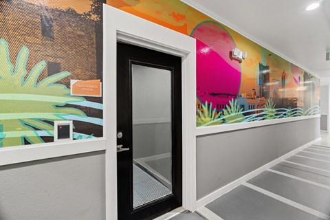A black door with a glass window is in the middle of a white wall with a colorful mural.