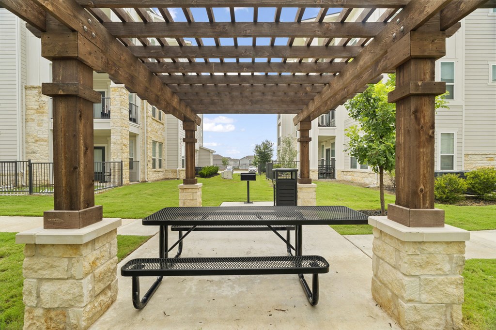 A wooden pergola with a black table underneath it.