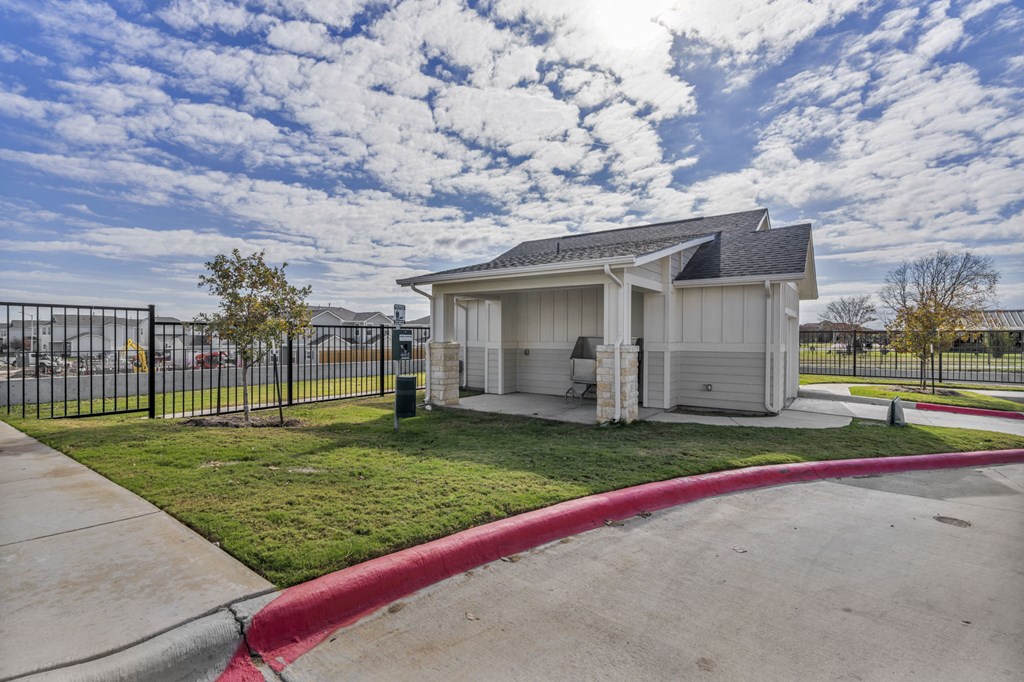 a small building with a fence around it and a grassy area with a driveway