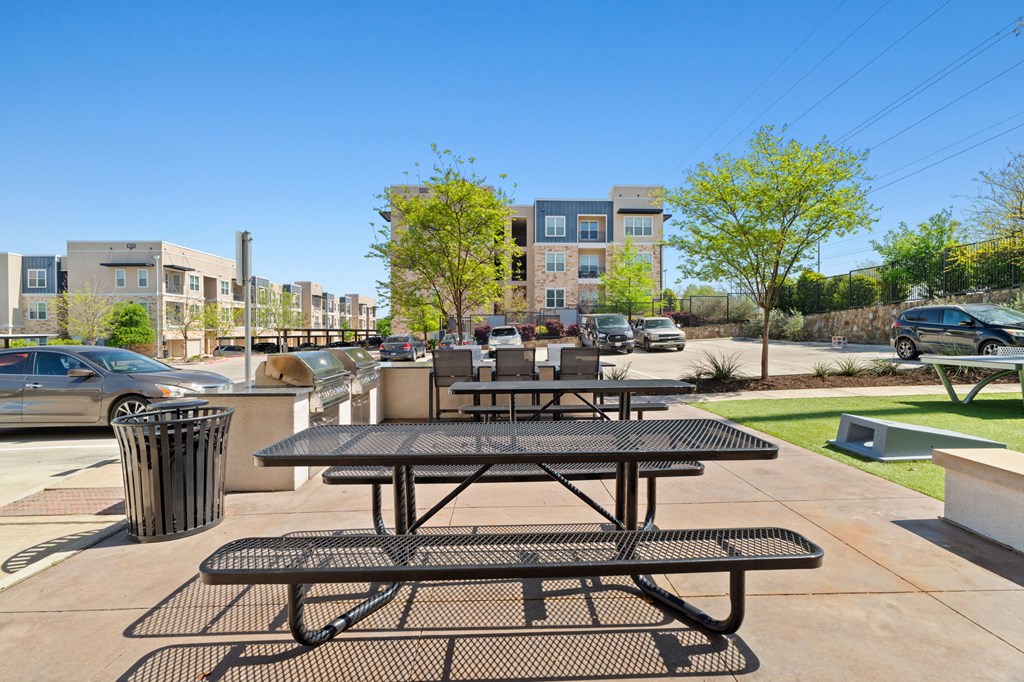 A black picnic table is in the foreground of a sunny day in a parking lot.