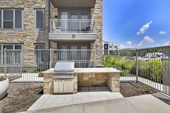 an outdoor kitchen with a grill and a table and chairs in front of an apartment building