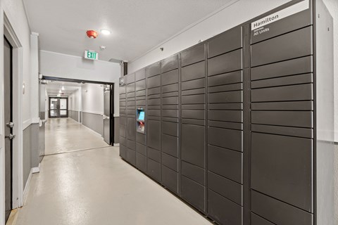 A long hallway with a wall of lockers on the right and an exit sign above.