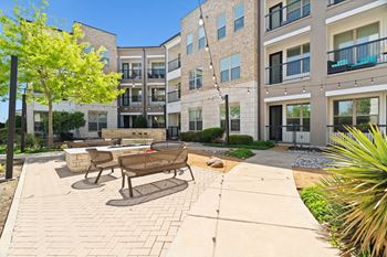 A sunny day at a modern apartment complex with a brick patio and seating area.