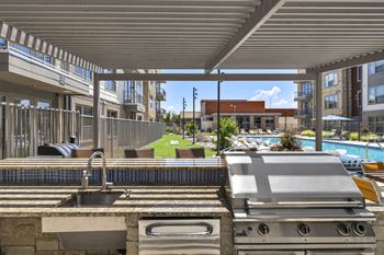 an outdoor kitchen with a grill and a sink and a pool in the background