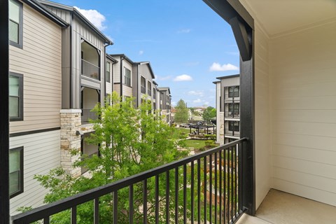 A balcony overlooks a courtyard with trees and a building in the background.