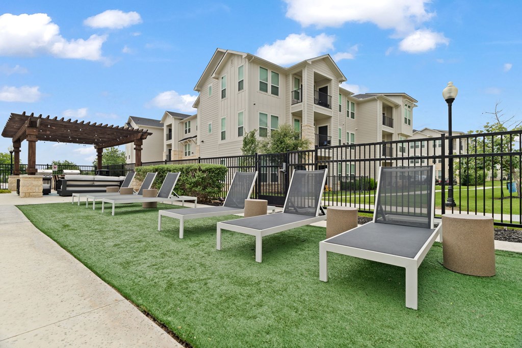A row of white and grey benches are lined up on a green lawn in front of a building.