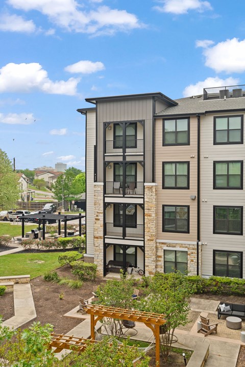 A modern apartment building with a balcony and a garden in front.