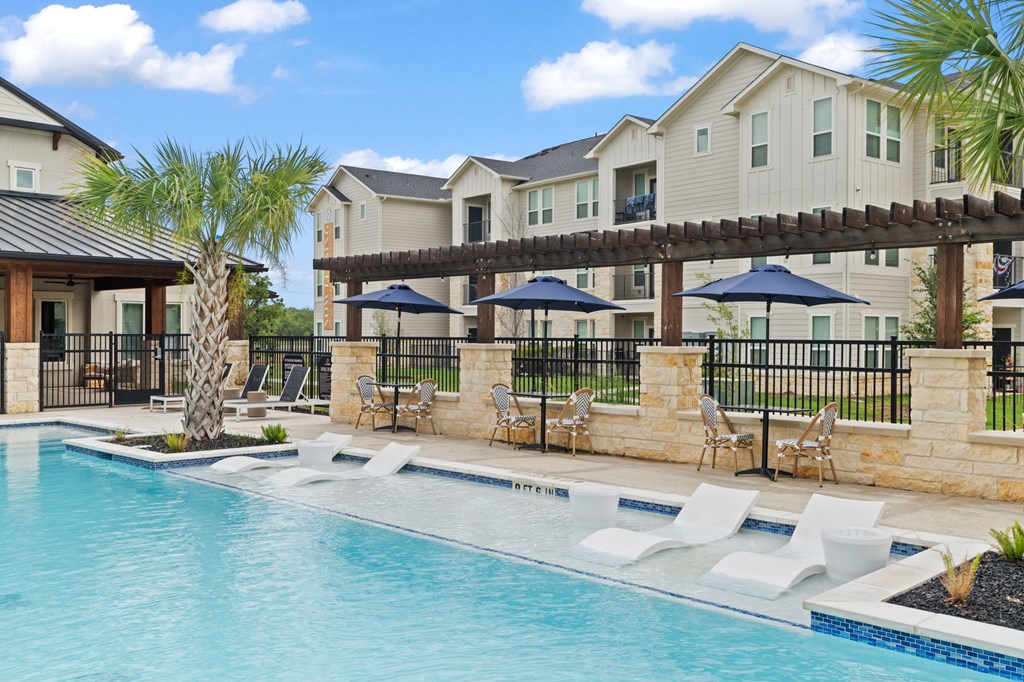 A pool surrounded by chairs and umbrellas with a building in the background.