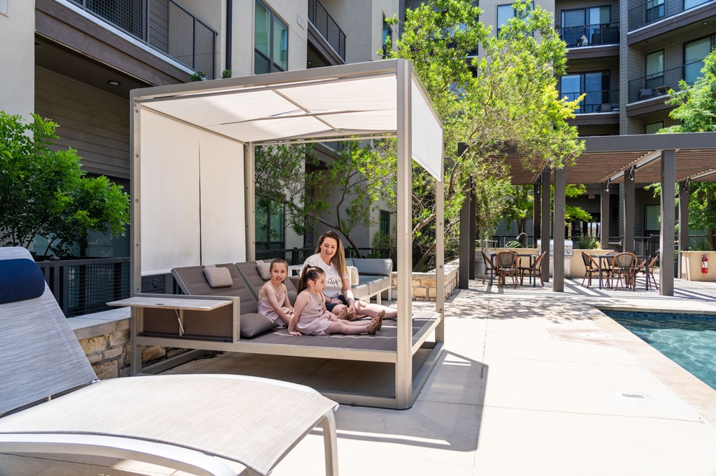 A woman and two children are sitting on a couch under a canopy on a patio.