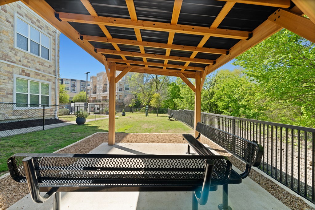 A wooden pergola with a black metal bench in front of a building.
