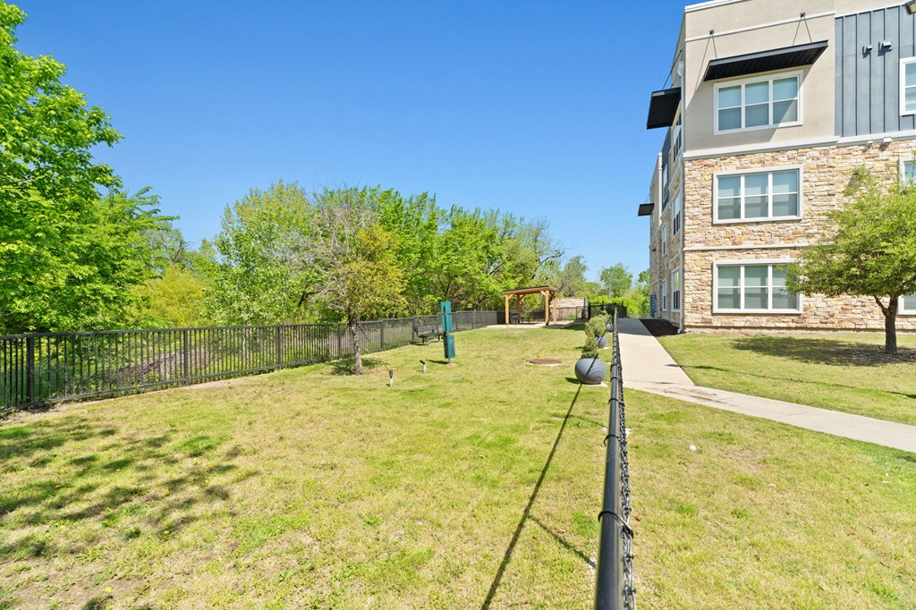 A grassy area in front of a building with a fence and trees.
