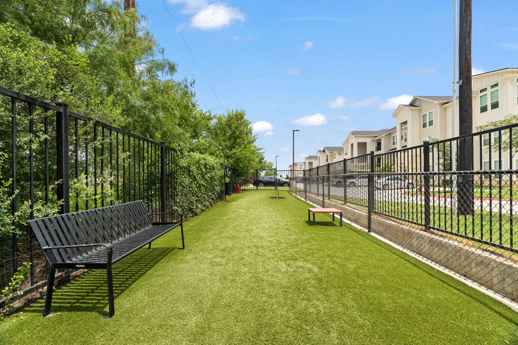 A black metal fence surrounds a green lawn with two benches.