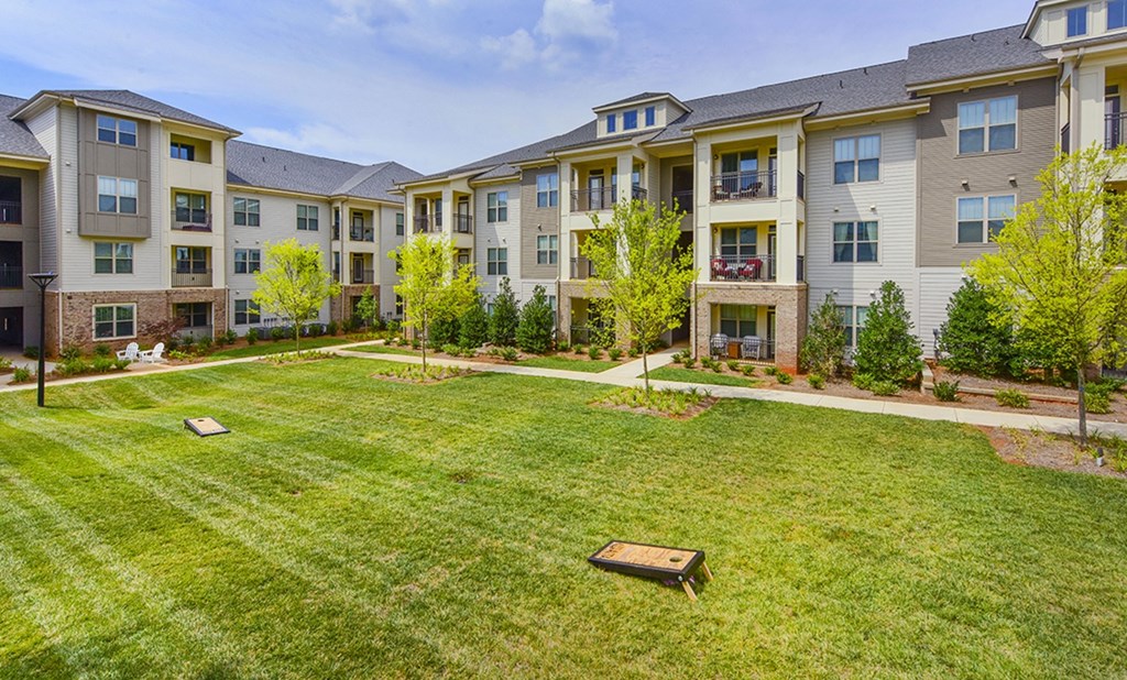 an apartment yard with grass and trees in front of an apartment building