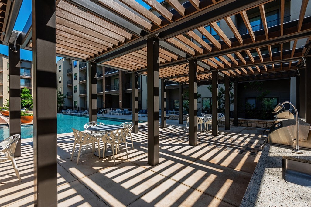 a covered patio with tables and chairs next to a pool