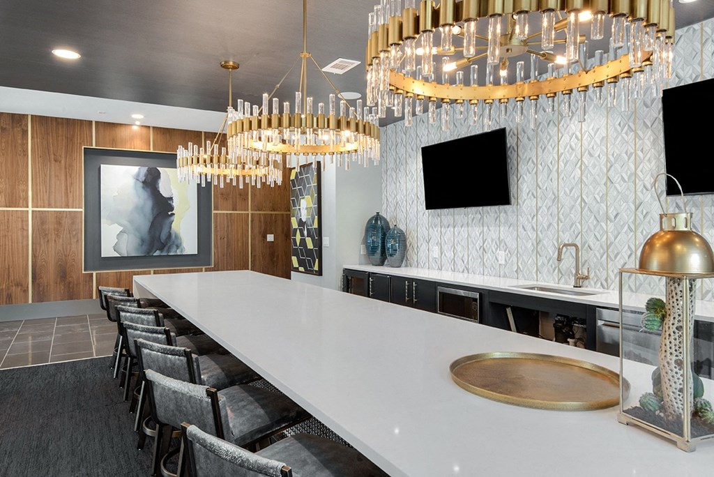 a kitchen with a long white counter and chairs and chandeliers