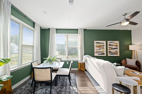 A living room with a white couch, a dining table with chairs, and a ceiling fan.