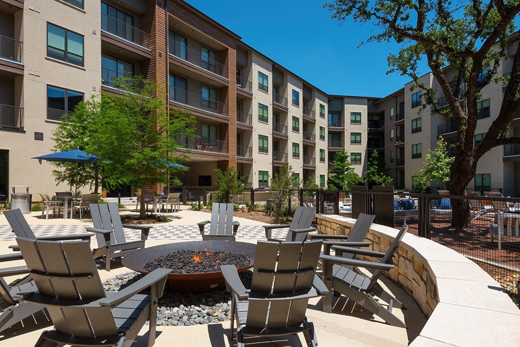 an outdoor patio with chairs and a fire pit in front of an apartment building