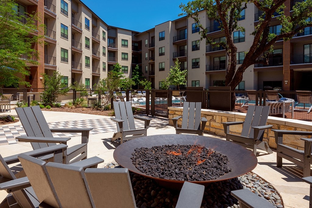 an outdoor patio with chairs and a fire pit in front of an apartment building