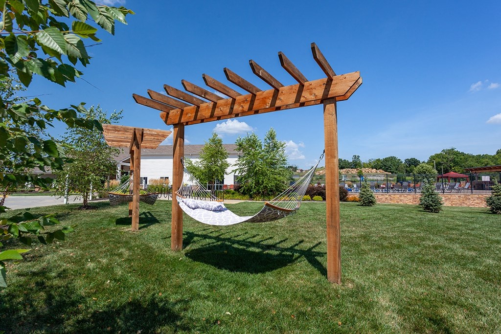 a hammock hanging under a wooden pergola in a park