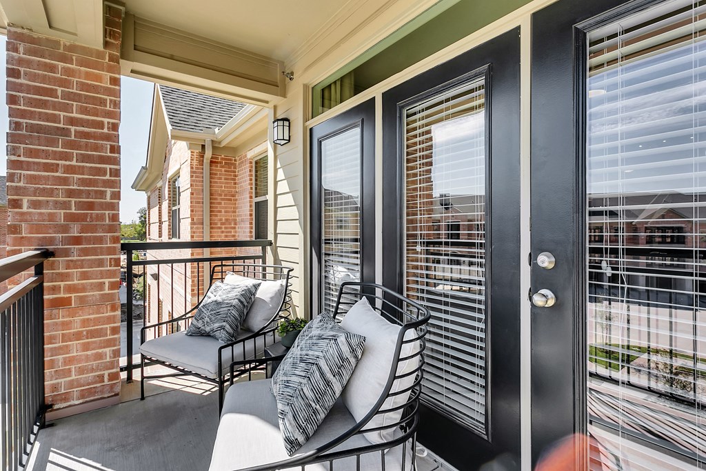 a balcony with a black door and two chairs with pillows