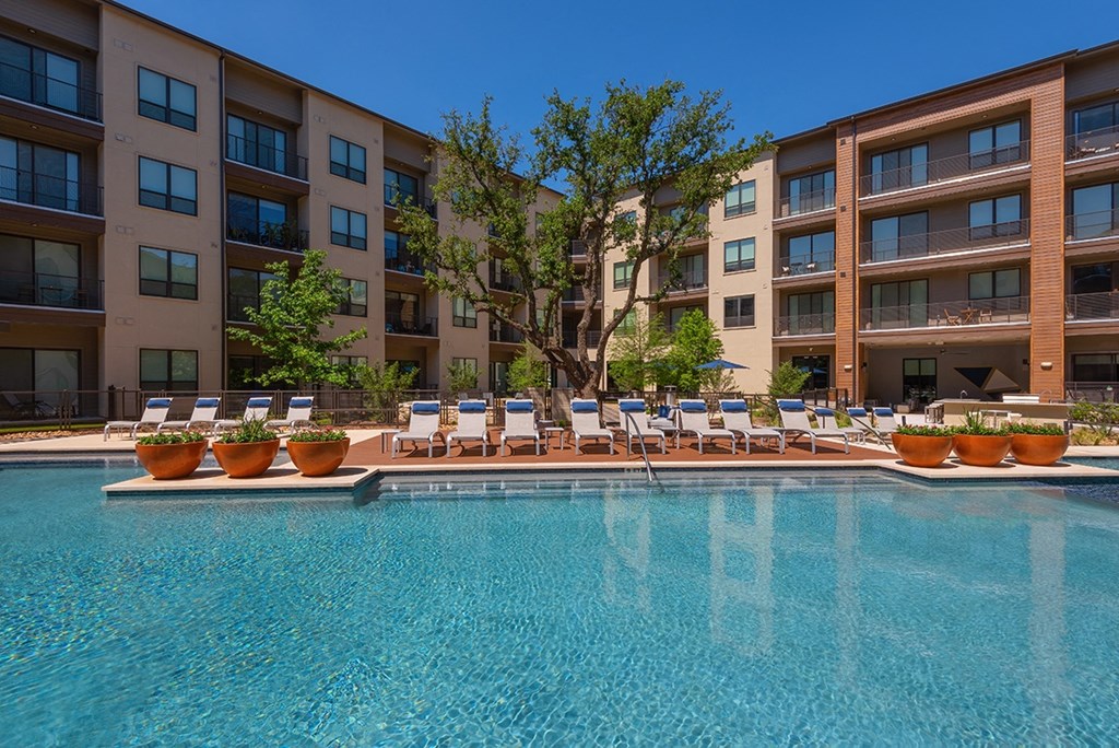 a swimming pool with lounge chairs in front of an apartment building