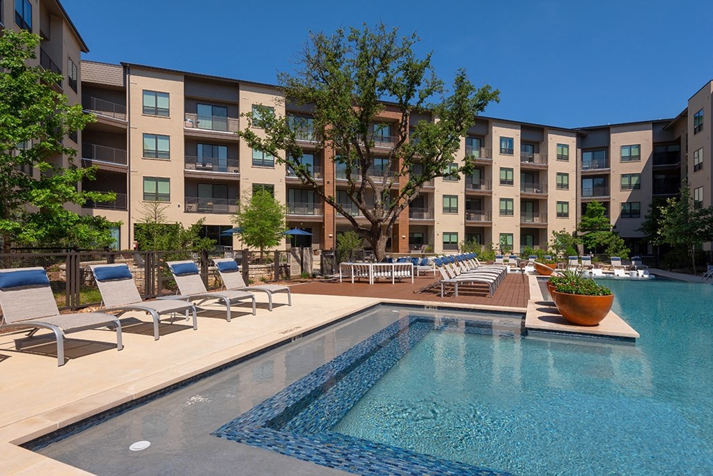 a swimming pool with lounge chairs in front of an apartment building