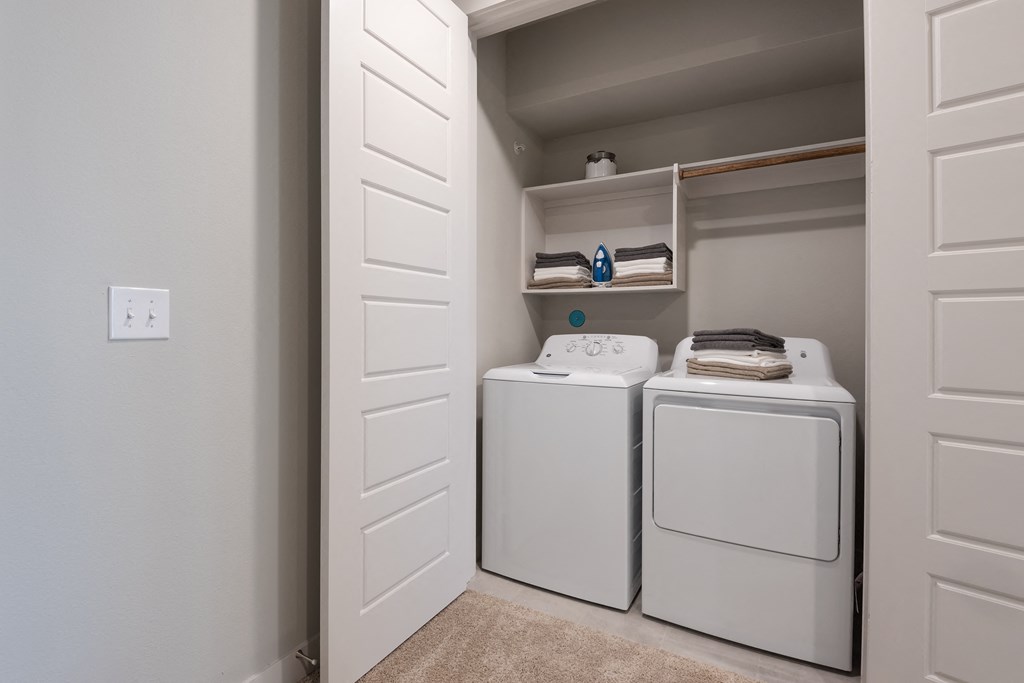 a washer and dryer closet in a laundry room with white appliances and shelves