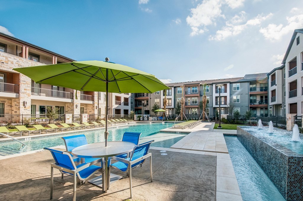 a pool with a table and chairs with an umbrella in front of an apartment building