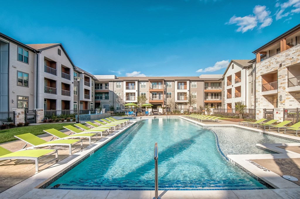 a swimming pool with yellow lounge chairs in front of an apartment building