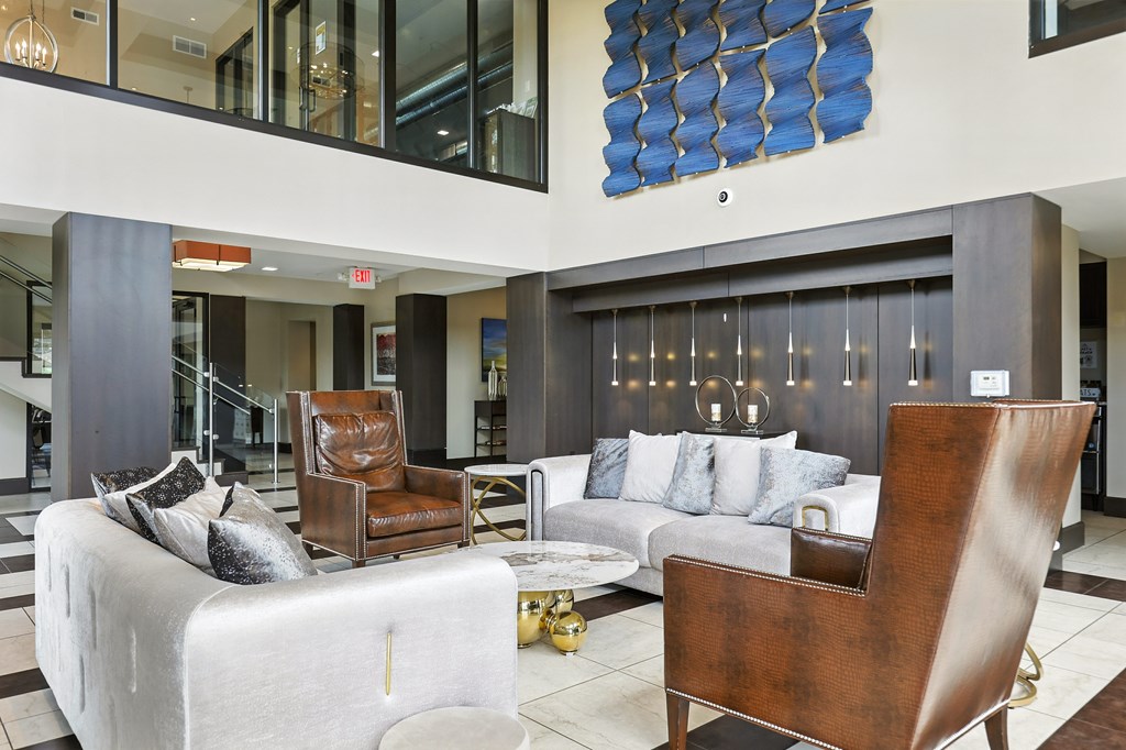 A modern living room with a white couch, a brown leather chair, and a blue abstract painting on the wall at Alinea Town and Country Luxury Apartments in Des Peres MO 63131..